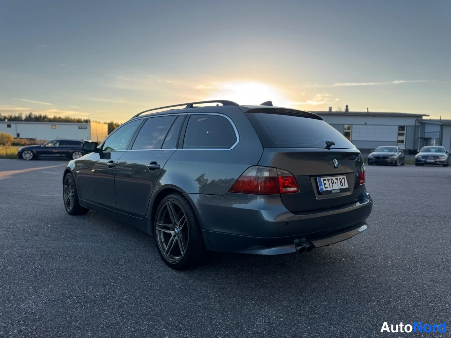 Takaviisto: Tummanharmaa BMW 5-sarjan farmari kulmatrista takaa vasemmalta, rekisteritunnus.