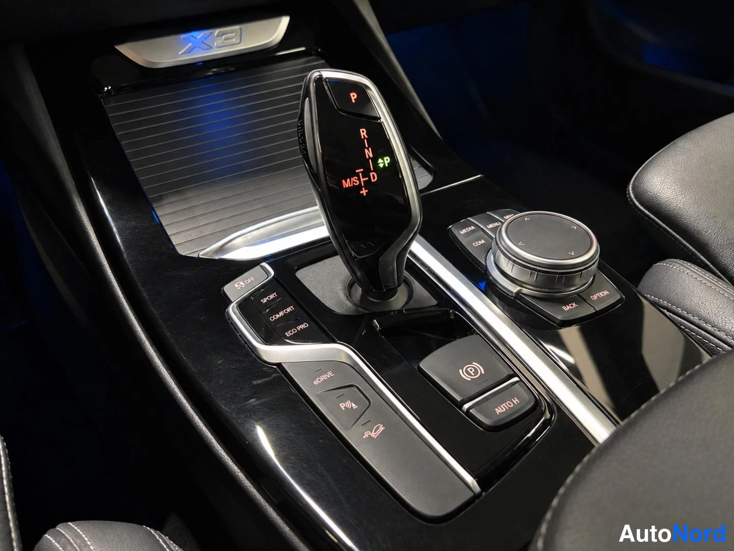 Muu: Lähikuva automaattivaihteiston valitsimesta ja iDrive-ohjaimesta, valitsimessa P R N D -asemat ja ajotilat SPORT, COMFORT ja ECO PRO.