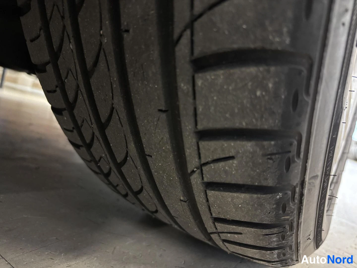 Yksityiskohta: Lähikuva auton renkaasta, jossa näkyy kulunut ja halkeillut kulutuspinta.