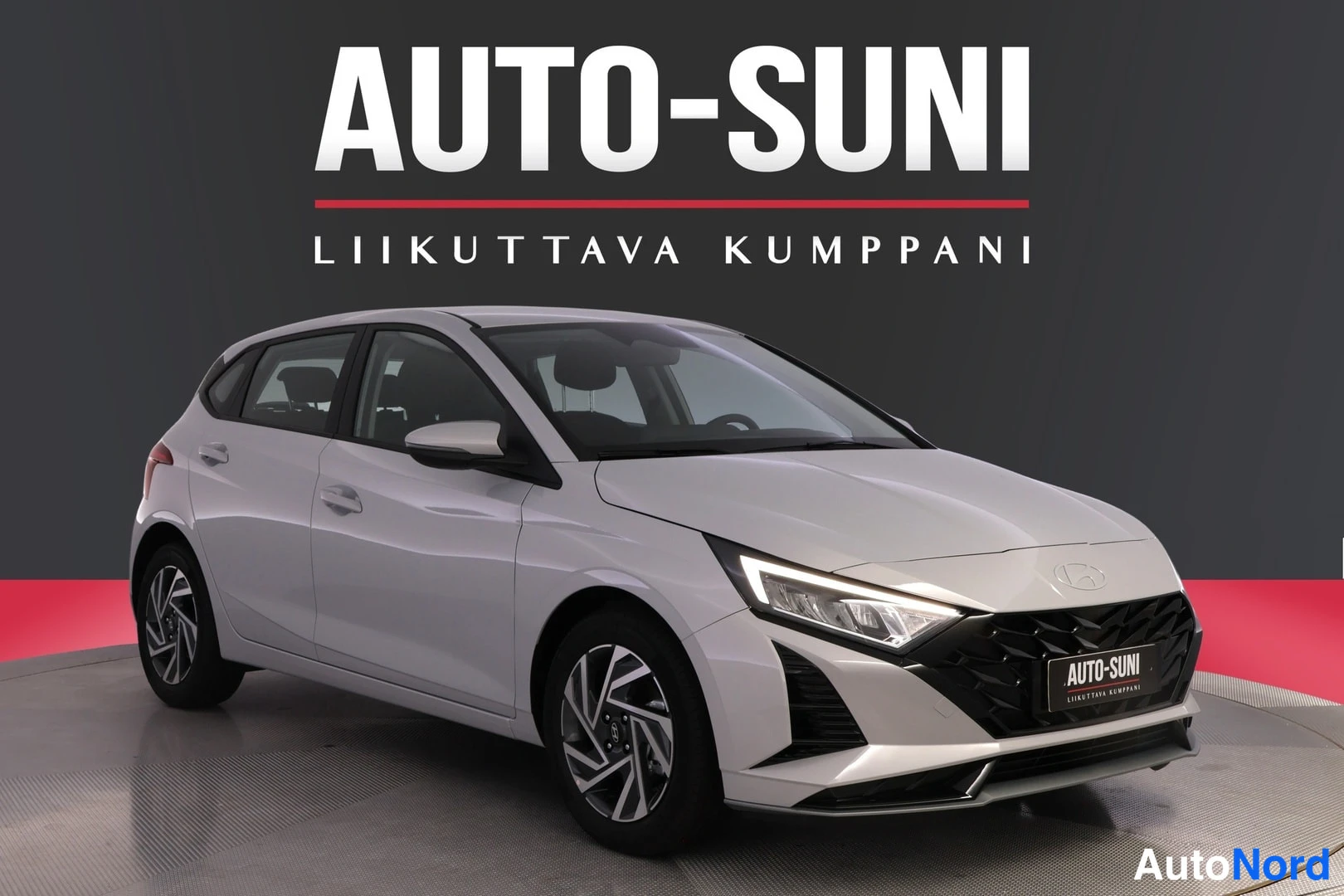 Etuviisto, nokka oikealle: Hyundai i20 viistosta edestä oikealta, vaaleanharmaa viistoperä näkyvissä tummassa studiossa.