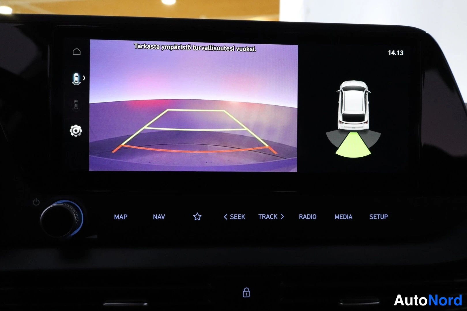 Muu: Auton infotainment-näyttö näyttää 360-kamerakuvan pysäköintitukiviivoilla ja tekstin 'Tarkasta ympäristö turvallisuutesi vuoksi.' Alapuolella näppäimet MAP, NAV