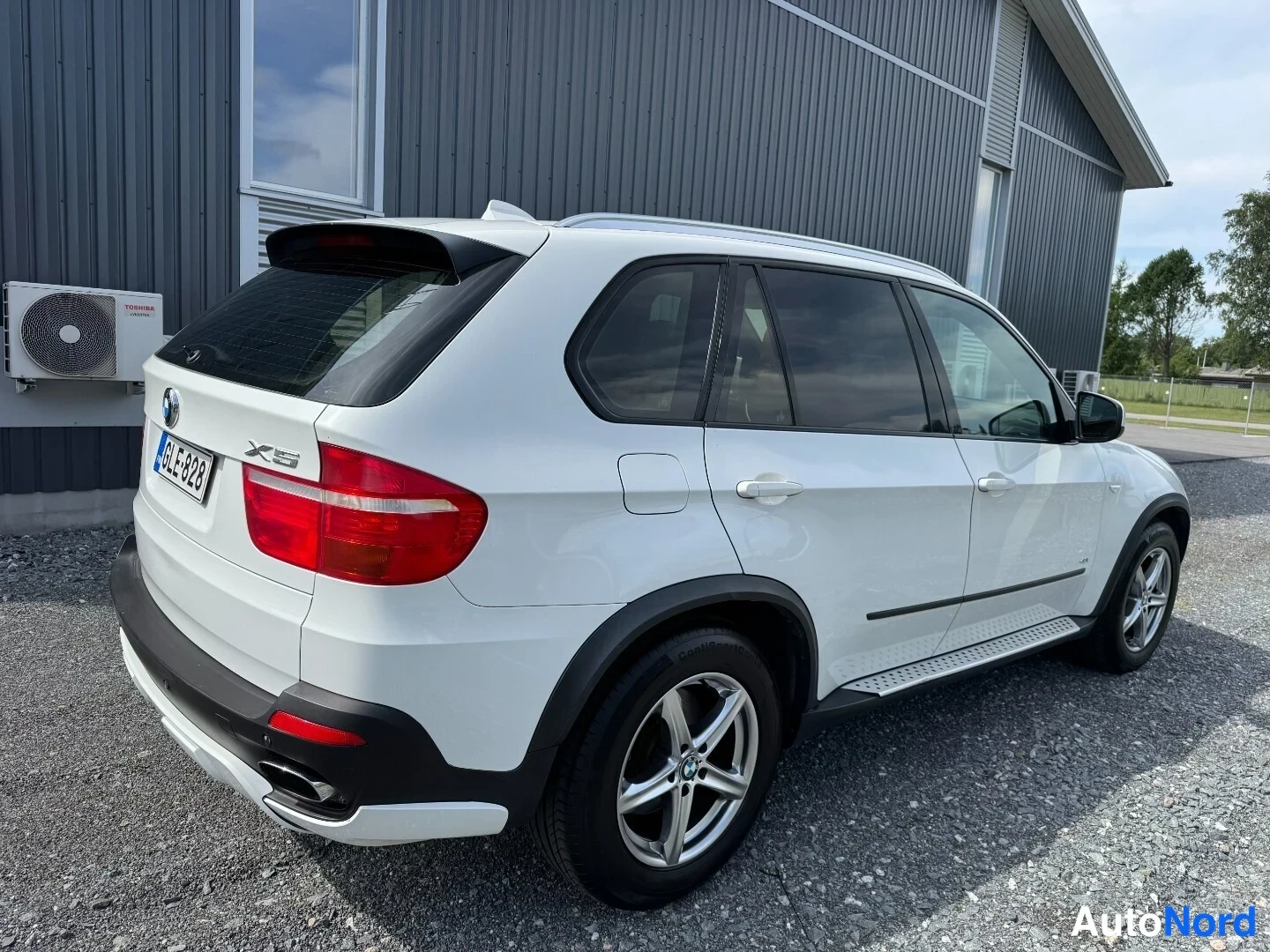 Takaviisto: BMW X5:n takakulmanäkyvä valkoinen SUV, rekisteritunnus, punaiset takavalot ja hopeavanteet.