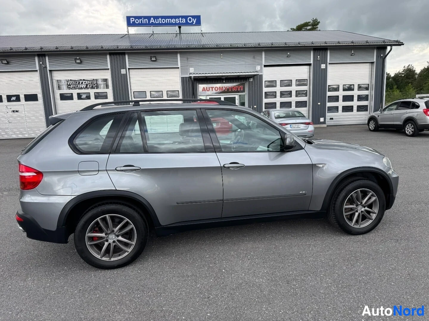Takaviisto: BMW X5:n takaosan ja sivuprofiilin näyttävä kuva autotallin edessä.