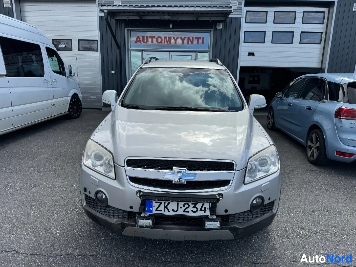 Edestä: Hopeanharmaan Chevrolet Captivan etunäkymä, rekisterikilpi ja komerialle asennettu LED-tanko.