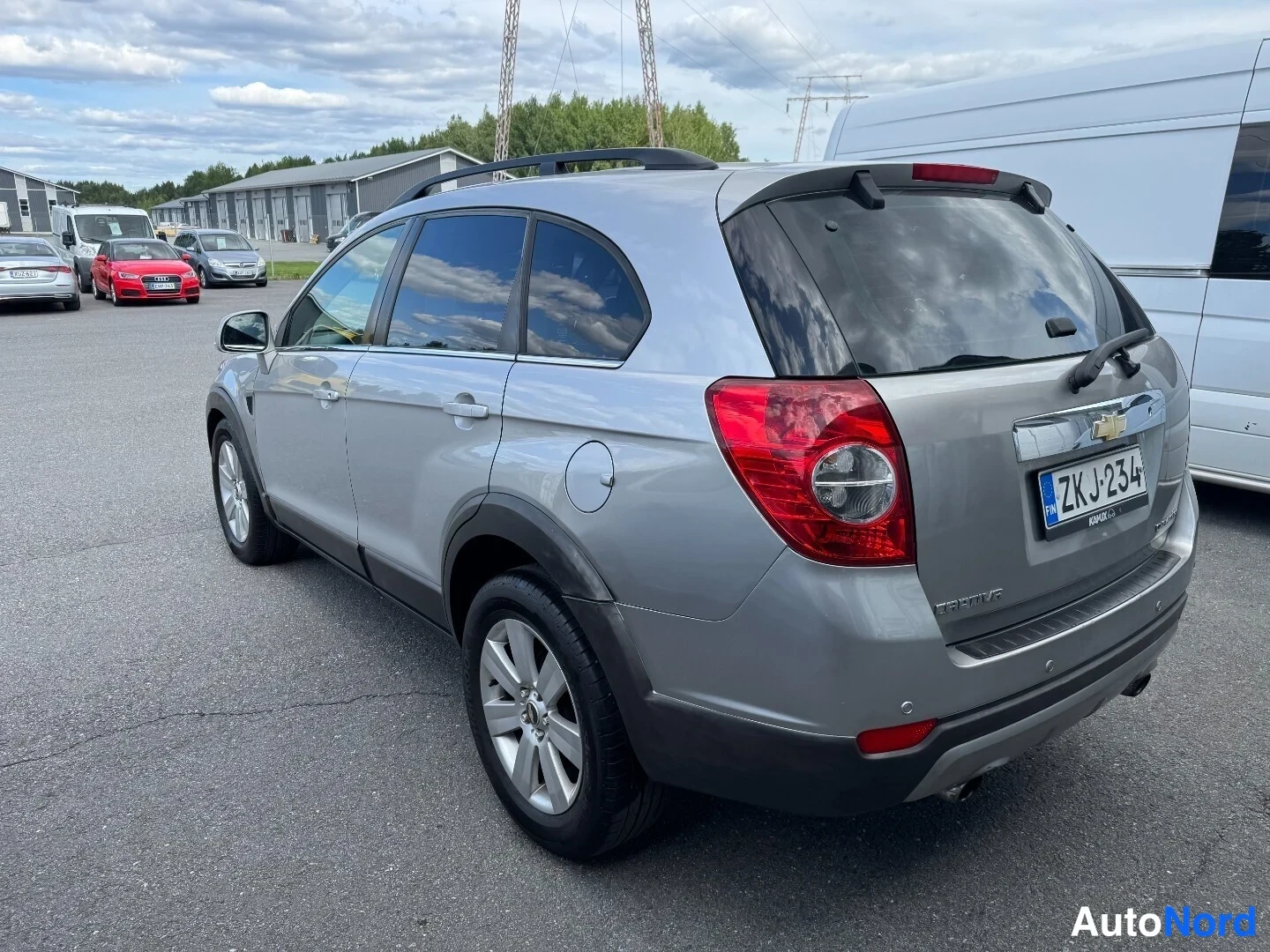 Takaviisto: Hopeanharmaa Chevrolet Captiva kolmeneljännesnäkymässä takaa vasemmalta, kattokaiteet ja rekisterikilpi näkyvät.