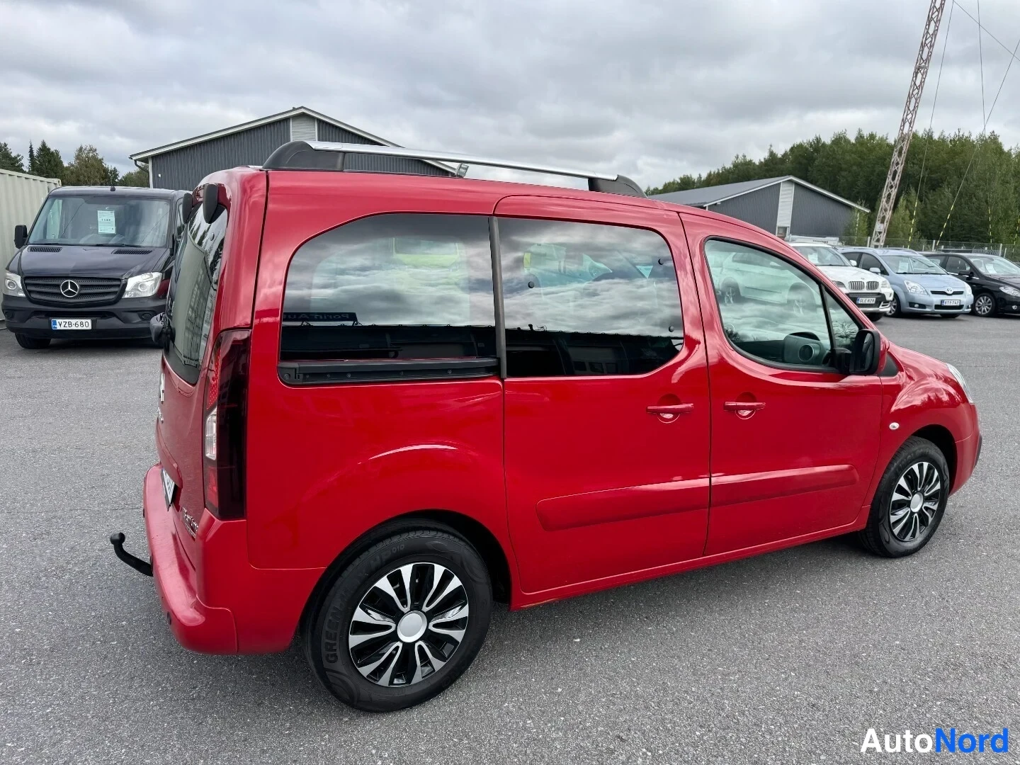 Sivulta: Punainen Citroën Berlingo sivulta oikealta päin; kattokiskot, liukuovet ja takimmainen pyörä näkyvät.