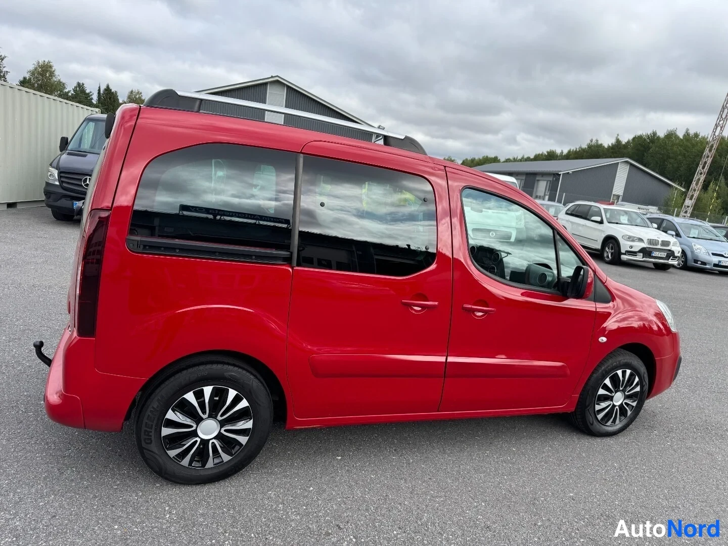Sivulta: Punainen Citroën Berlingo sivulta oikealta päin; kattokiskot, liukuovi ja molemmat oikeanpuoleiset pyörät näkyvät.