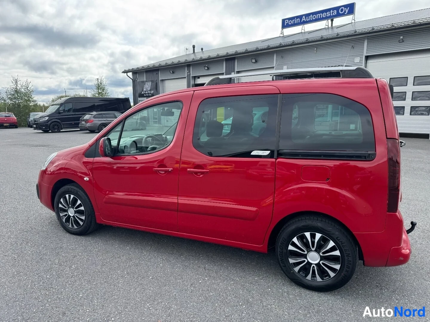 Etuviisto, nokka vasemmalle: Punainen Citroën Berlingo -pakettiauto sivusta etunasokulmasta, kattotelineet ja hopeavanteet näkyvissä.