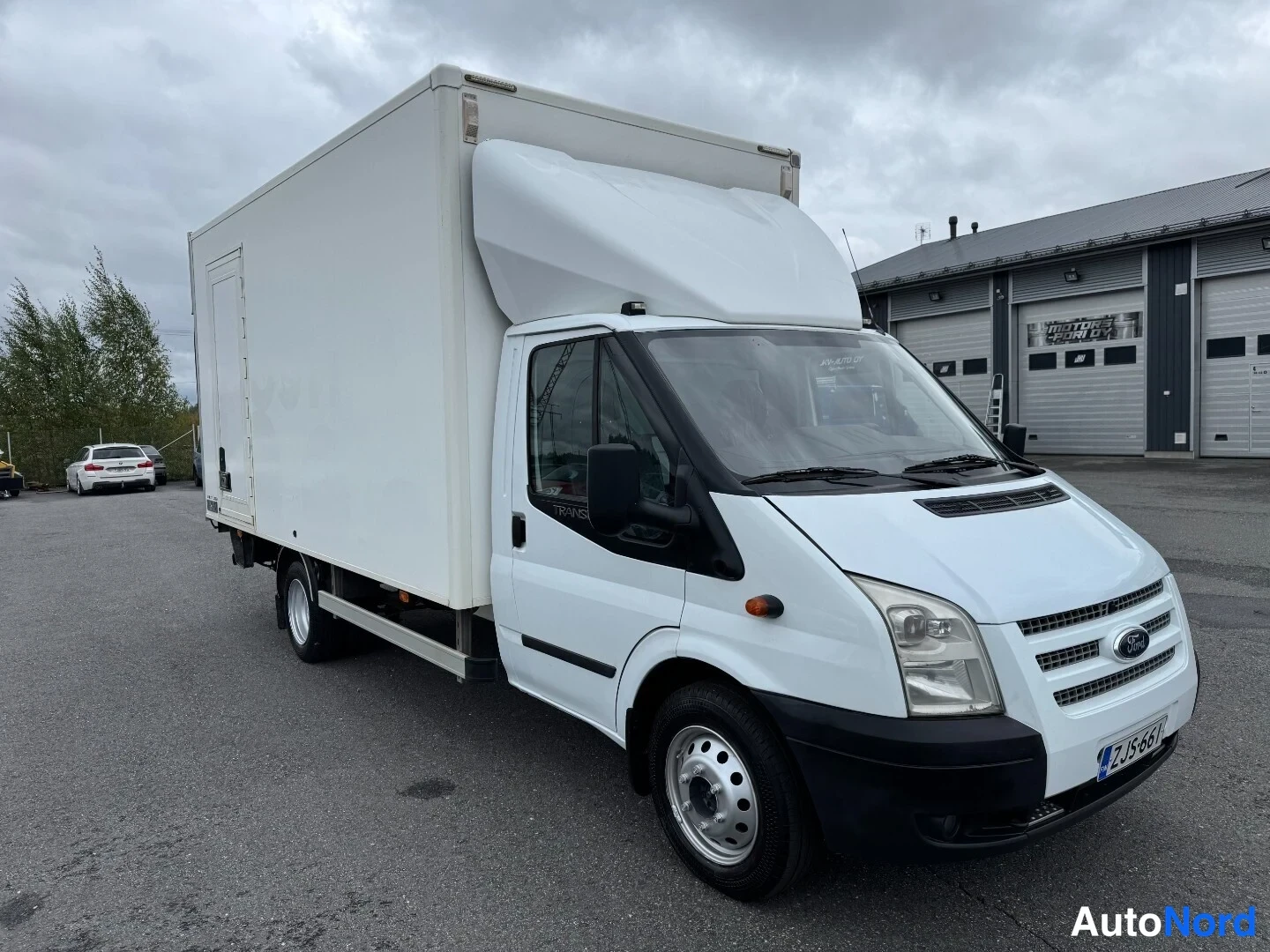 Etuviisto, nokka oikealle: Valkoinen Ford Transit-kuorma-auto etuviistosta vasemmalle, Ford-merkki ja rekisterikilpi näkyvissä.