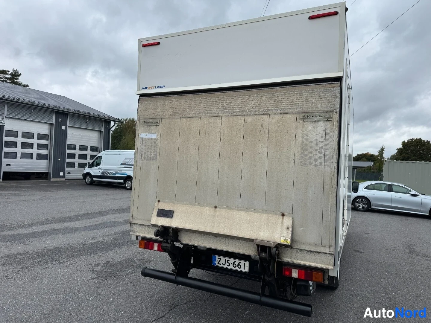 Takaa: Pakettiauton perä takaa päin: valkoinen lavallinen kuormatilaa, nosturilaita ja rekisterikilpi.