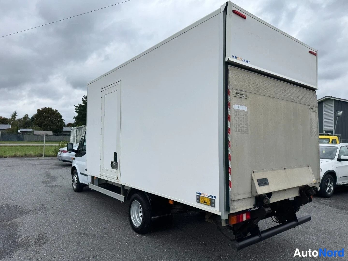 Takaviisto: Valkoinen Ford Transit -pakettiauto vasemmasta takaosasta kuvattuna: laaja kuormatila, sivuovi ja takana nosturilaita.
