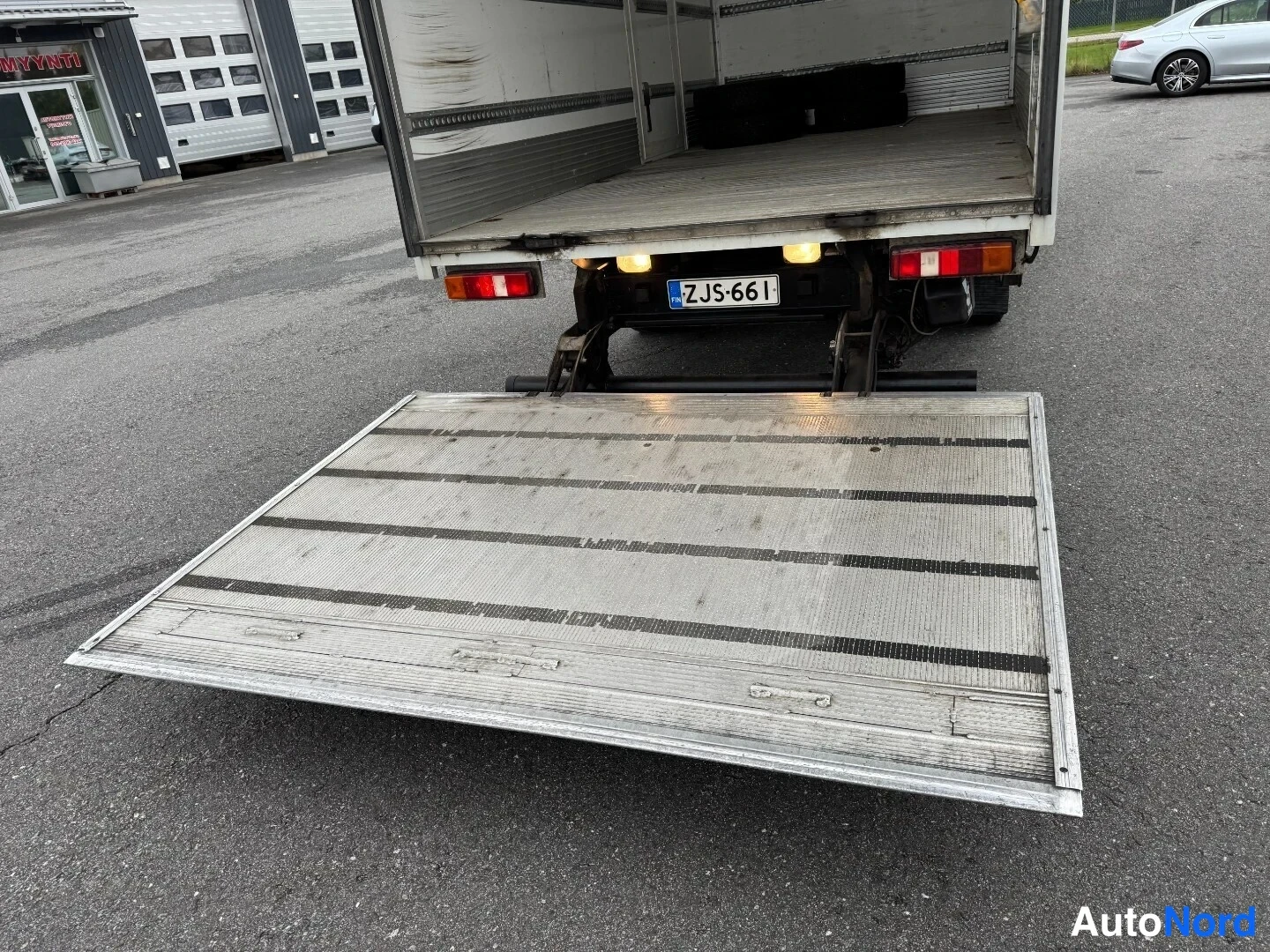 Takaa: Takanäköalakuva kuorma-auton takaa: takaosan hydraulinen lastauslava on laskettu maahan ja autotilan sisäpuolelle on jätetty kiinteä kiinteä kiinteä kiinteä kii