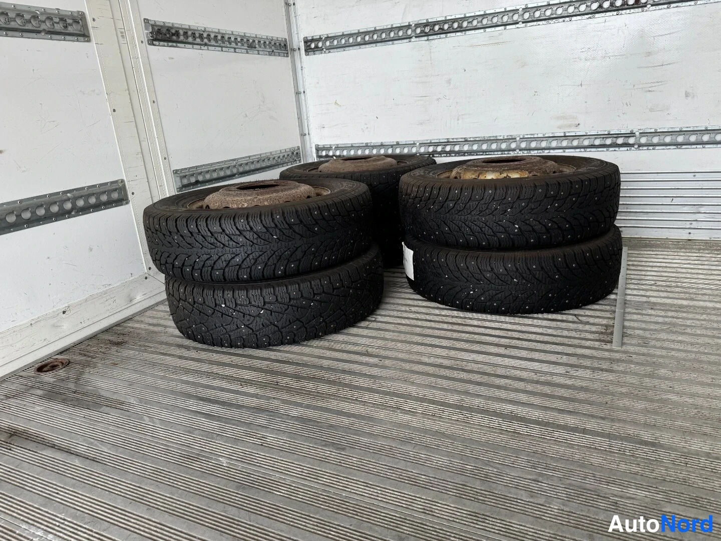 Muu: Neljä nastarenkaita pinossa pakettiauton lavan uritetulla alumiinipohjalla.