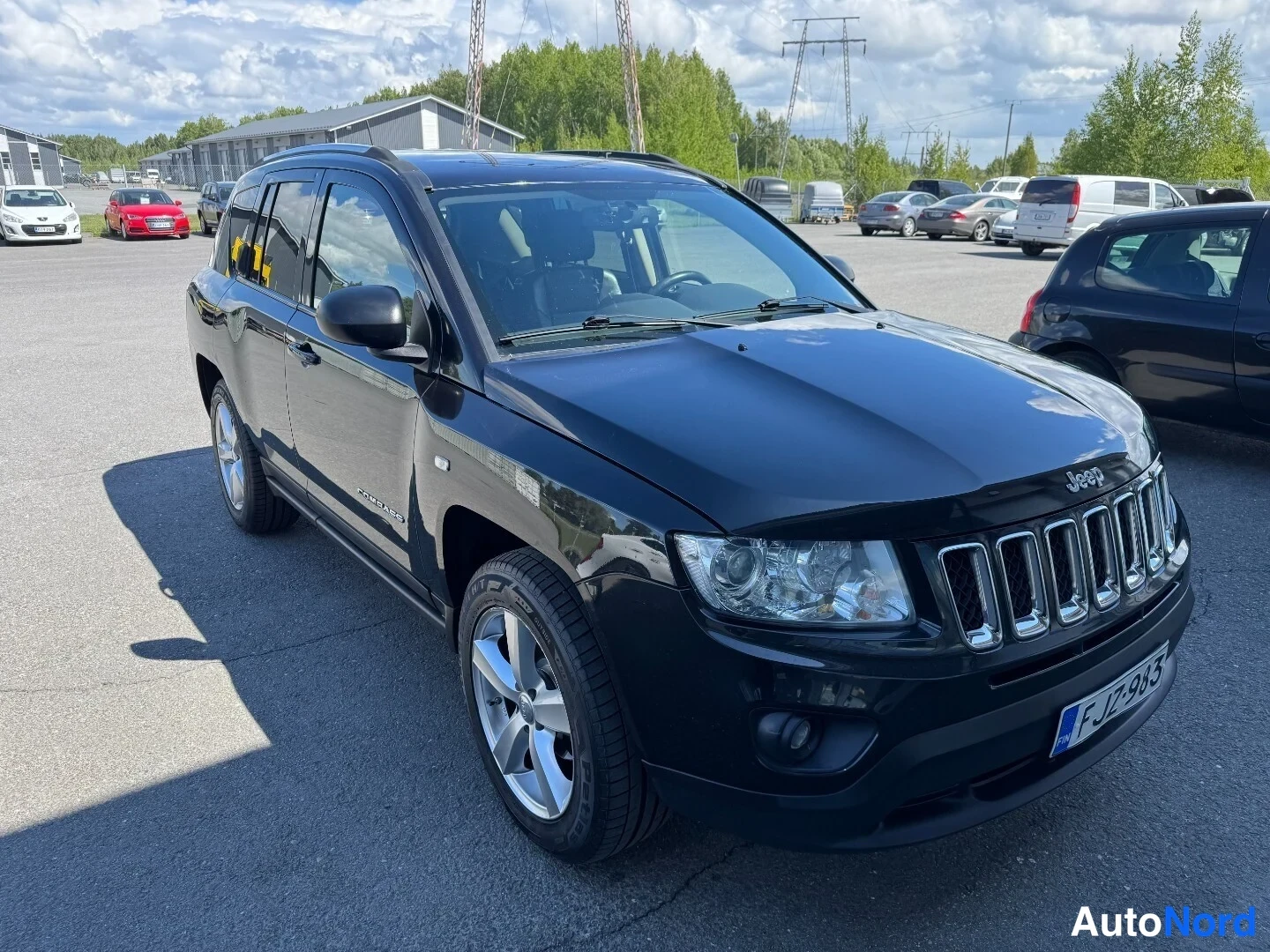 Etuviisto, nokka oikealle: Musta Jeep Compass kolmivartaloa etukulmasta, rekisterissä, parkkeerattuna autopaikalle.