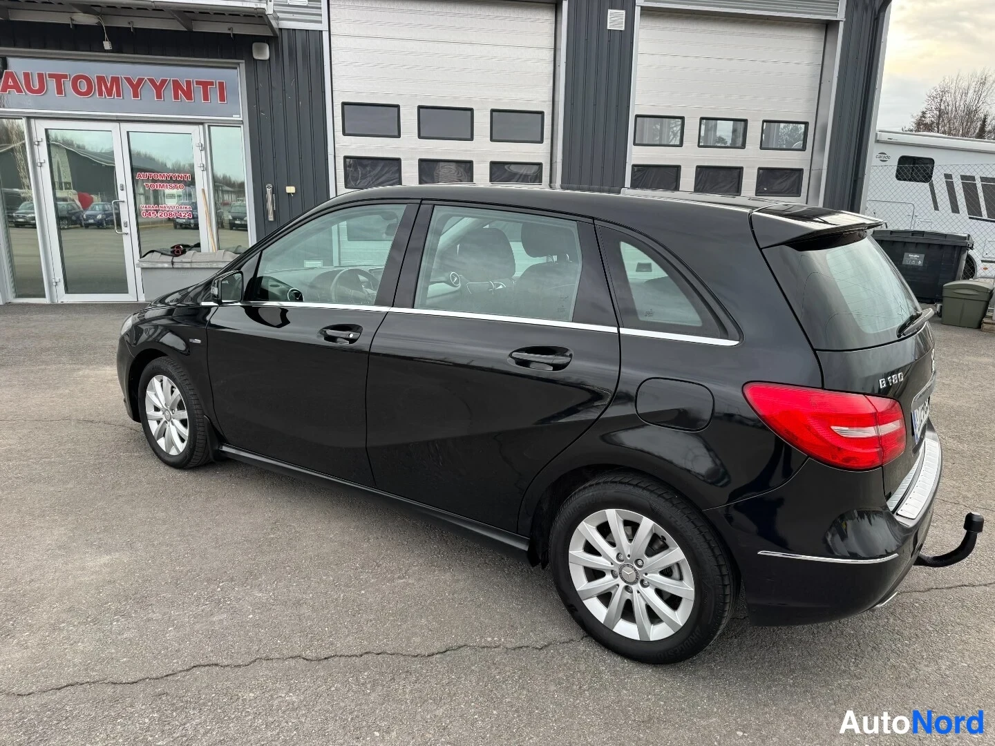 Takaviisto: Mustan Mercedes-Benz B-sarjan farmariauton takaosan ja vasemman sivun kolmasosakuva autoliikkeen pihalla.
