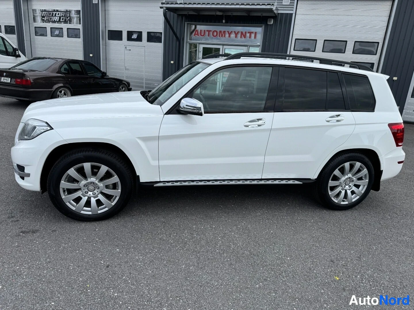 Etuviisto, nokka vasemmalle: Valkoinen Mercedes-Benz GLK -maastoauto sivulta etuosasta kuvattuna autonmyyntihallin edessä.