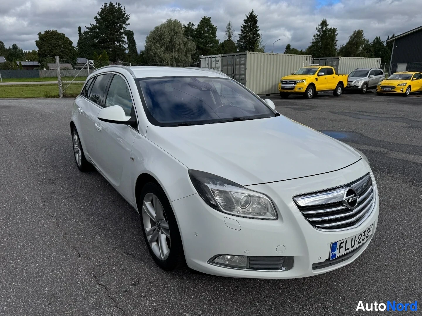 Etuviisto, nokka oikealle: Valkoinen Opel Insignia Sports Tourer -farmari kolmiseneljännes-etunäkymässä, keula oikealla, parkkipihalla.