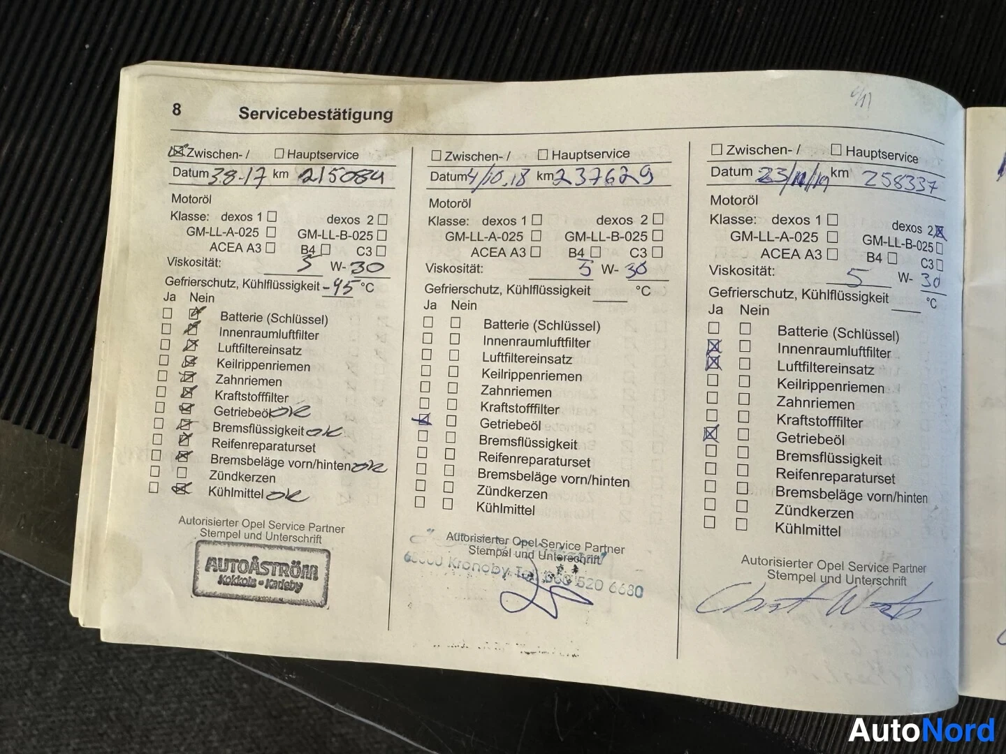 Asiakirja: Avattu Servicebestätigung-sivu 8, jossa kolme käsin täytettyä huoltoa lukemineen ja AutoÅström-korjaamon leima.