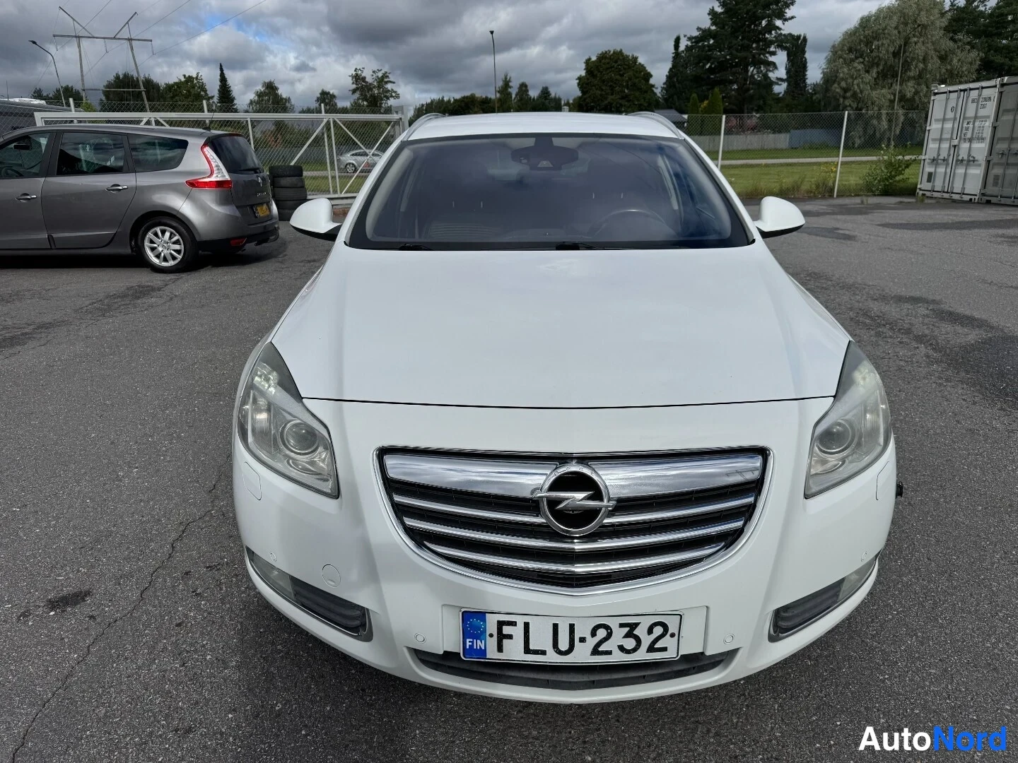 Edestä: Valkoisen Opel Insignian etunäkymä suoraan edestä, jolloin etusäleikkö, ajovalot ja rekisterikilpi näkyvät.