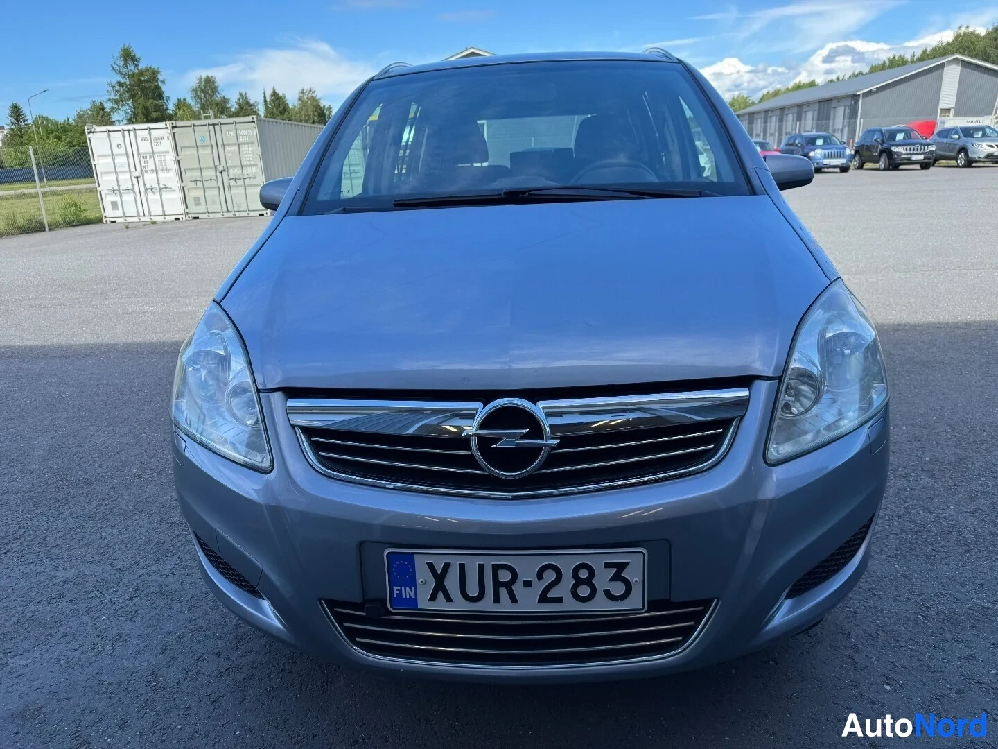 Edestä: Harmaansininen Opel Zafira suoraan edestä, Opel-merkki etusäleikössä, rekisterikilpi.