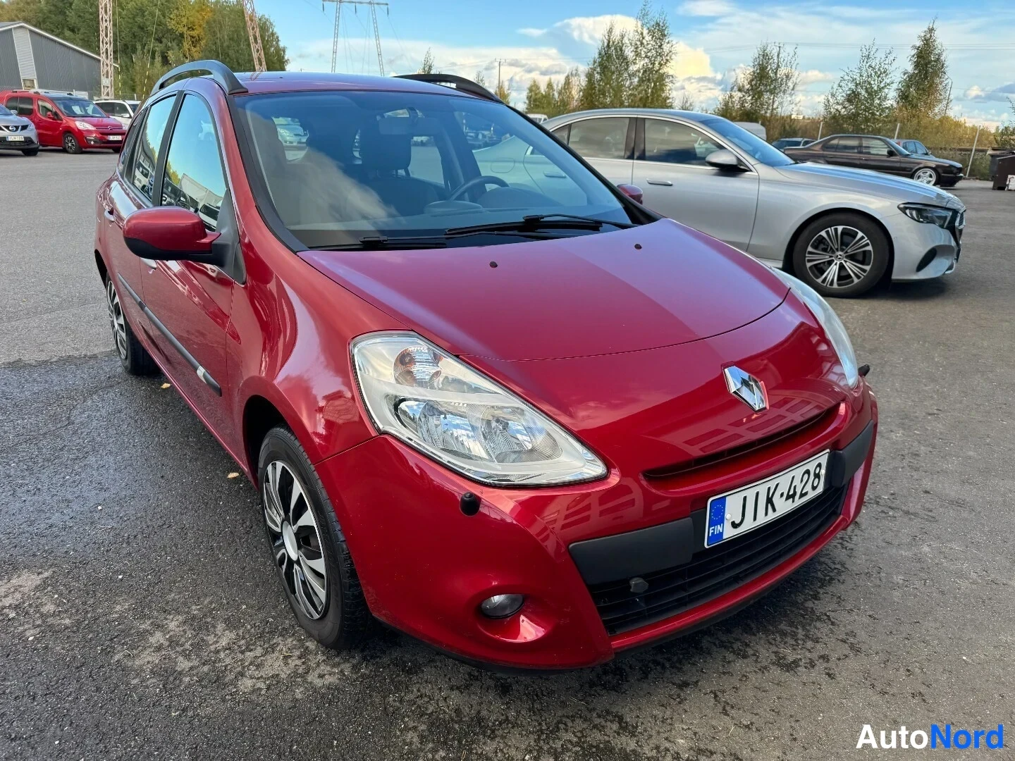Etuviisto, nokka oikealle: Punainen Renault Clio farmari kolmivartinäkymässä edestä oikealta, rekisterikilpi.