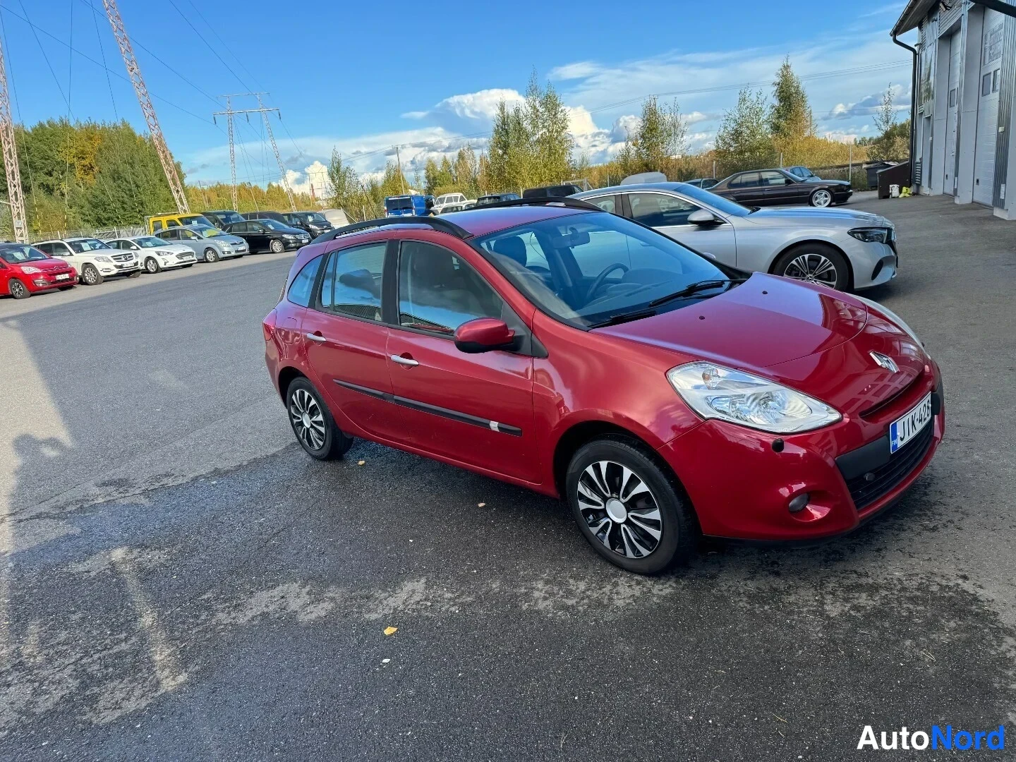 Etuviisto, nokka oikealle: Punainen Renault Clio farmari kolmivartinäkymässä edestä oikealta, rekisterikilpi.
