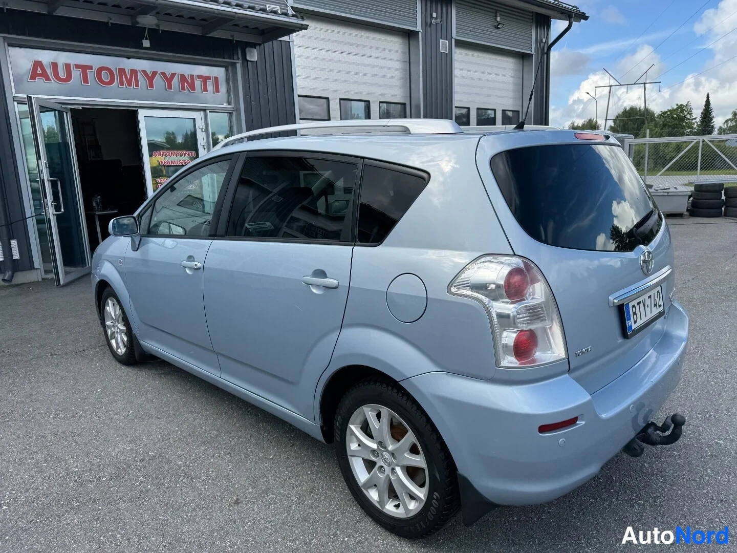 Takaviisto: Toyota Corolla Verso takaa viistosti vasemmalta, vaaleansininen koritila ja rekisterikilpi.