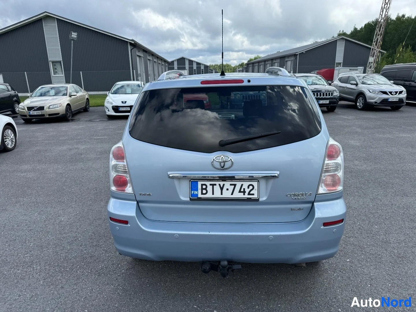 Takaa: Sinertävä Toyota Corolla Verso takaa kuvattuna, rekisterikilpi ja vetokoukku näkyvissä.