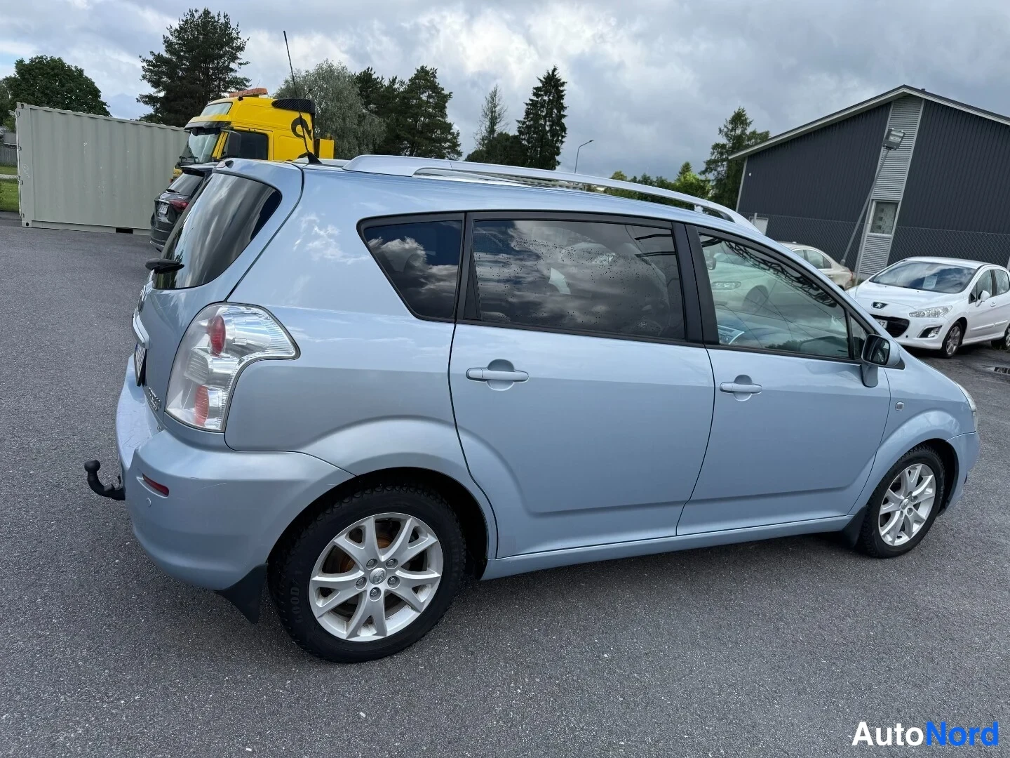Takaviisto: Toyota Corolla Verso -farmarikorinen takaa ja sivulta kuvattuna, vaaleansininen, kattokaiteet ja kevytmetallivanteet näkyvissä.