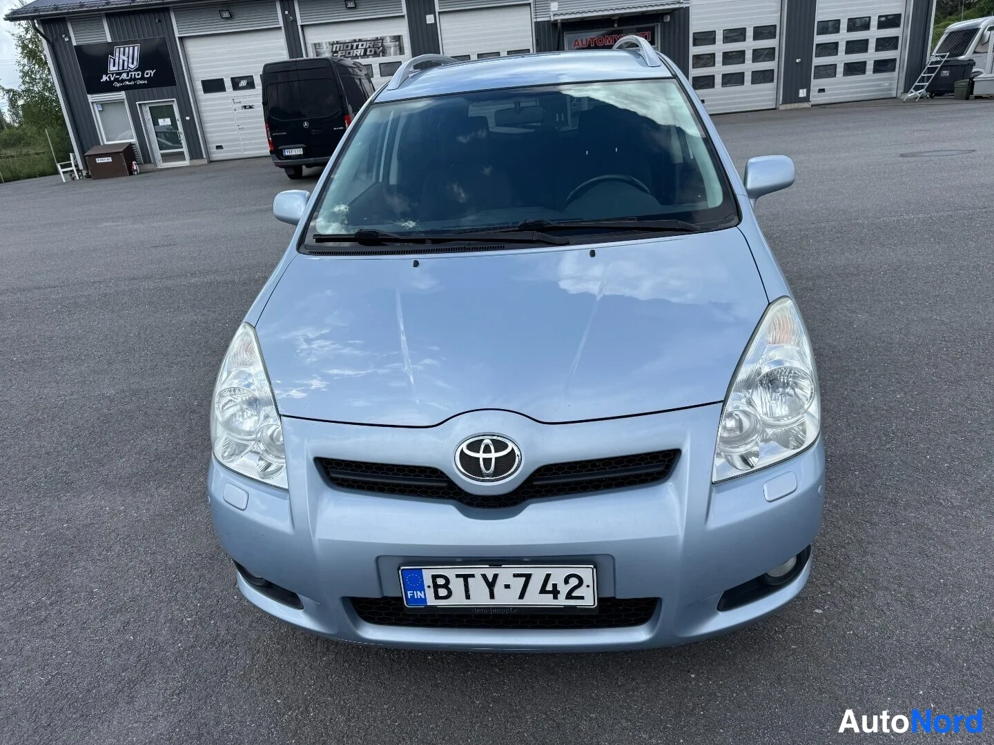 Edestä: Toyota Corolla Verso -henkilöauto edestä, vaaleansininen koriväri, rekisterikilpi.