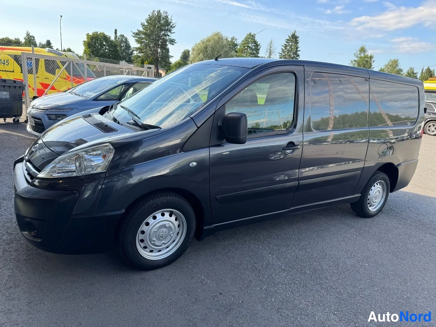 Etuviisto, nokka vasemmalle: Toyota Proace -pakettiauto tummanharmaana sivulta kolmanneltakulmalta edestä vasemmalta, teräsvanteet ja tummat ikkunat.