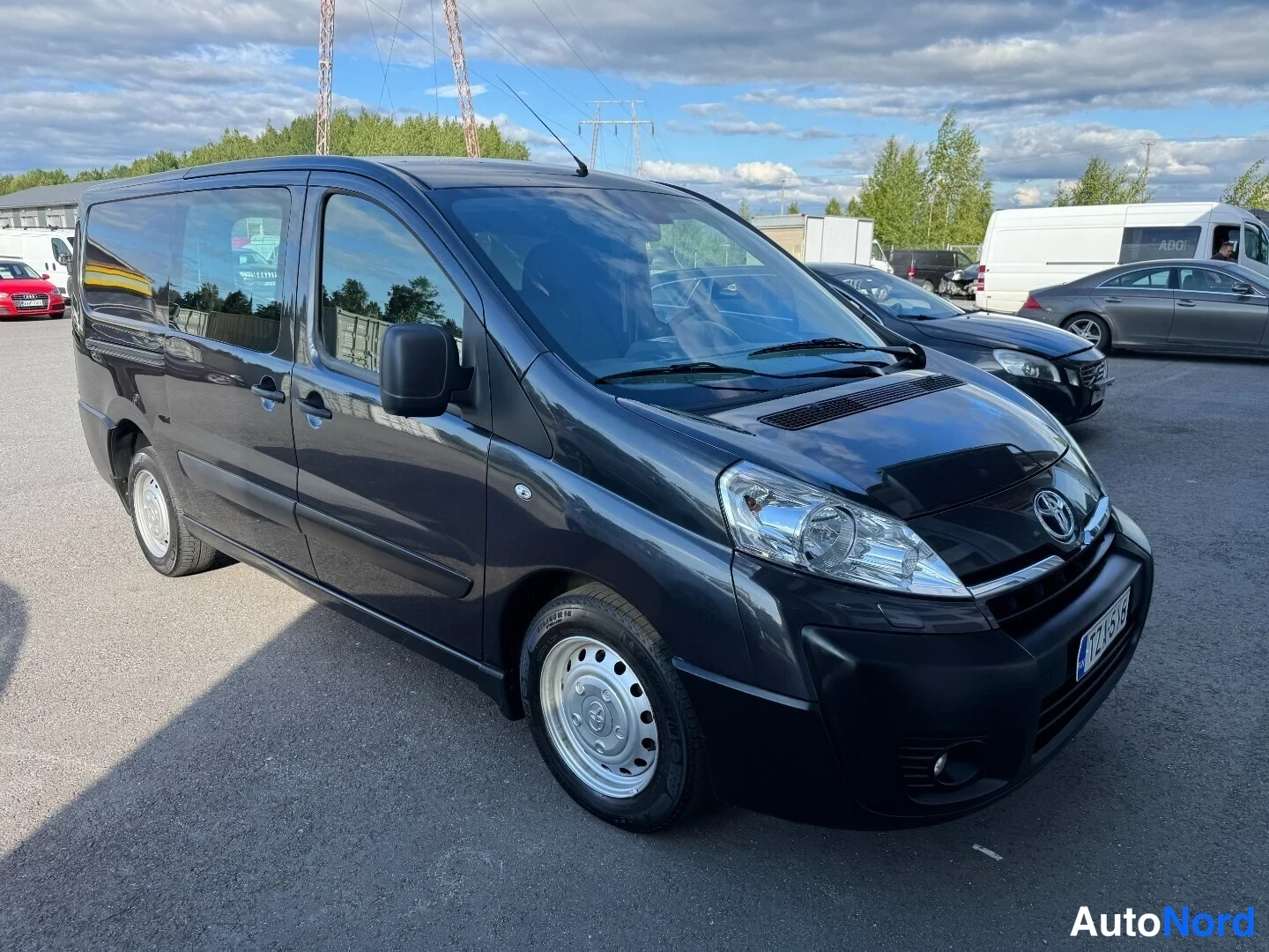 Etuviisto, nokka oikealle: Tummanharmaa Toyota Proace -pakettiauto etuviistosta oikealta, valot ja etupuskuri näkyvät, kevytmetallivanteet.