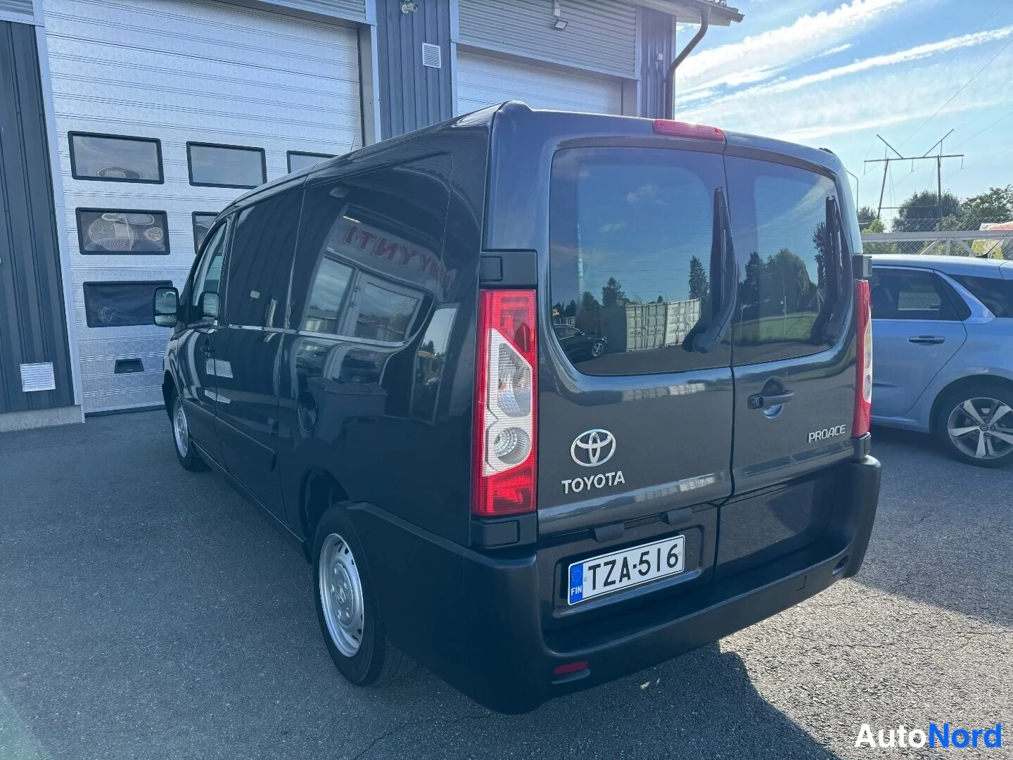 Takaa: Tummanharmaa Toyota Proace suoraan takaa, peräovet, Toyota- ja Proace-tekstit sekä rekisteri näkyvät.