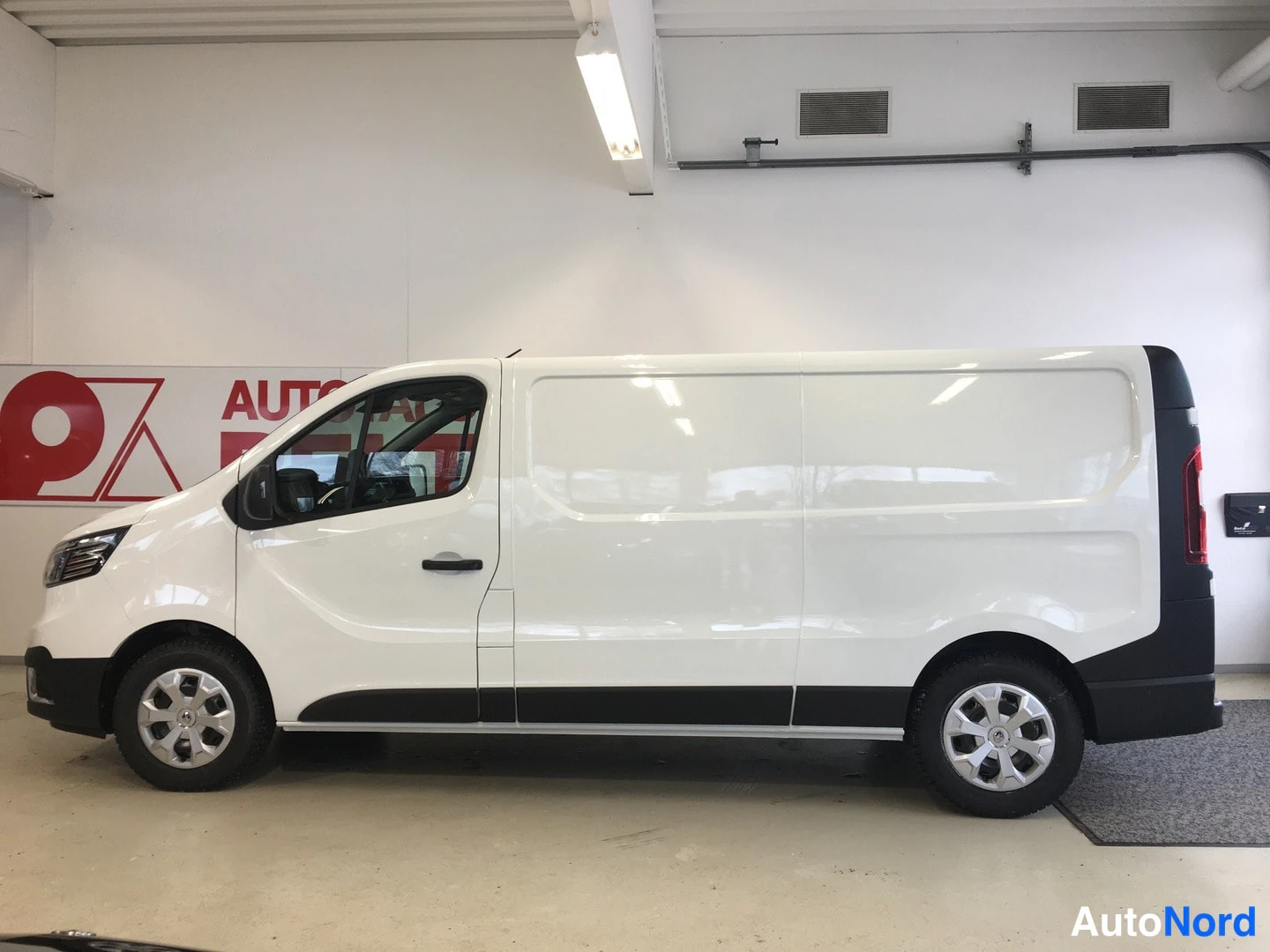 Etuviisto, nokka vasemmalle: Renault Trafic -pakettiauto sivulta, valkoinen koripaneelein ja mustilla alakehyksillä.