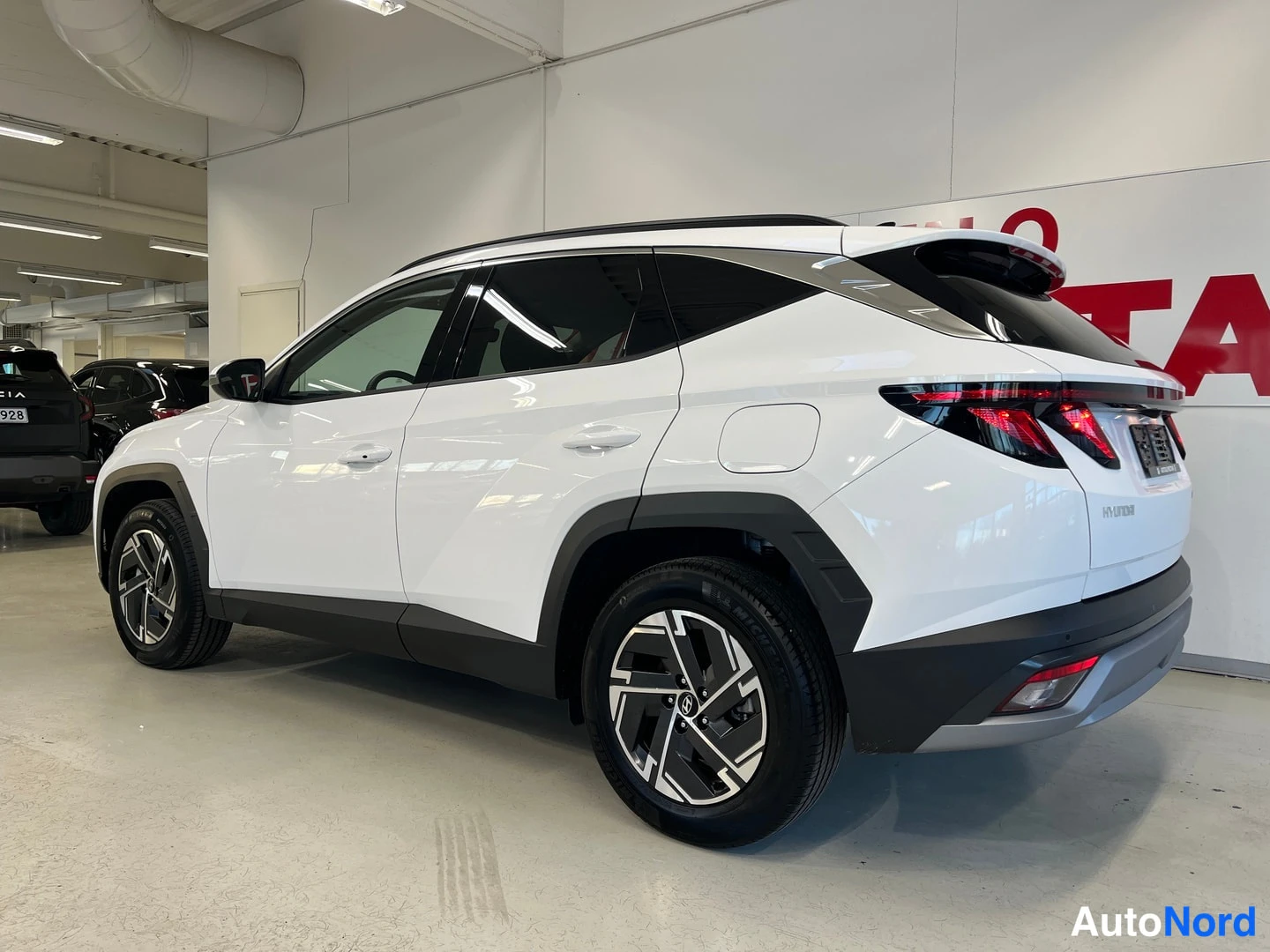 Takaviisto: Hyundai Tucson 1.6 T-GDi Plug-in Style 2025 – valkoinen, takaosa ja oikea kylki kuvattuna sisätiloissa