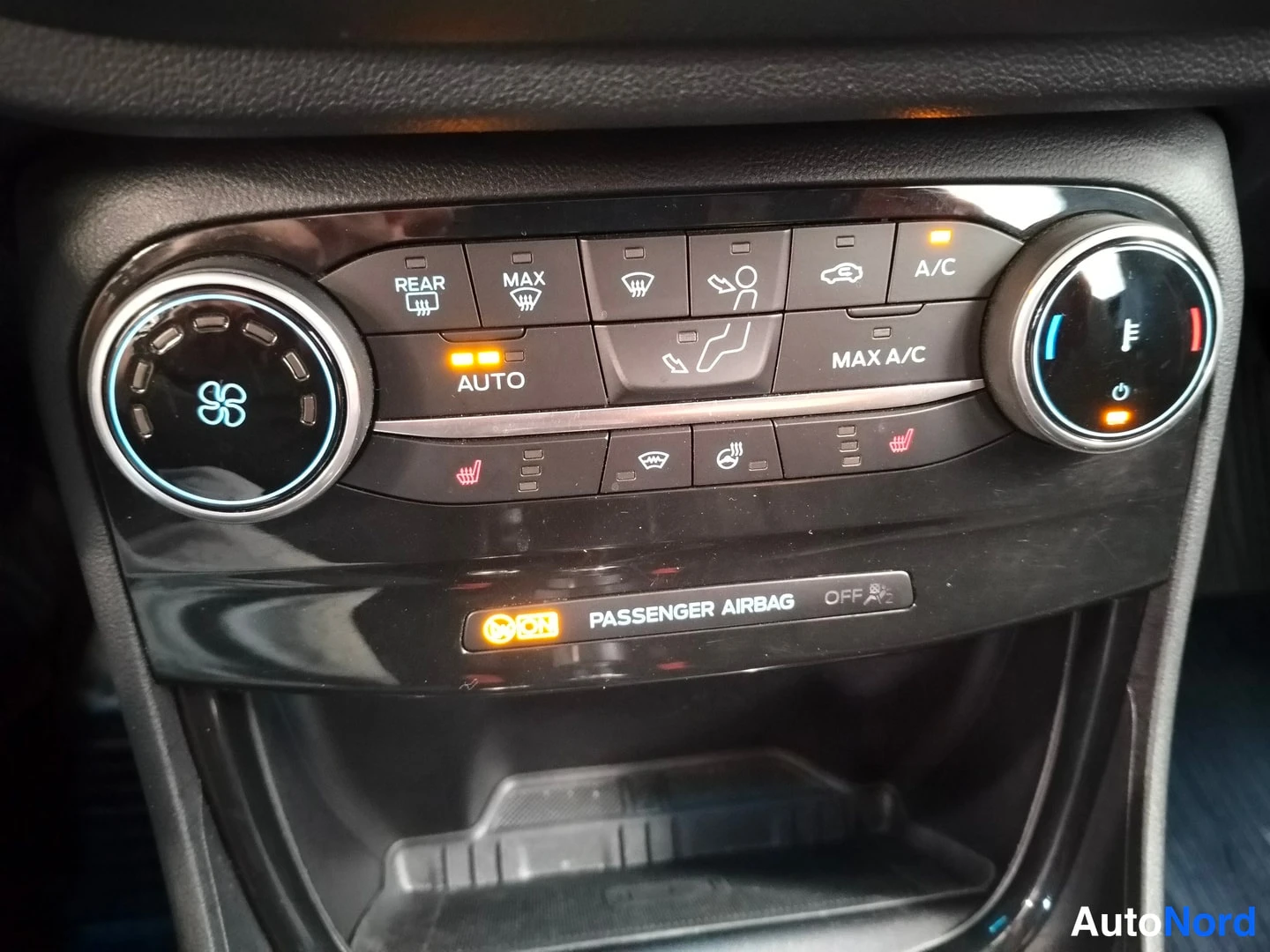 Yksityiskohta: Ilmastointilaitteen hallintapaneeli lähikuva: nappien tekstit REAR, MAX, AUTO, MAX A/C, A/C sekä lukkojen symbolit; alapuolella teksti PASSENGER AIRBAG OFF.