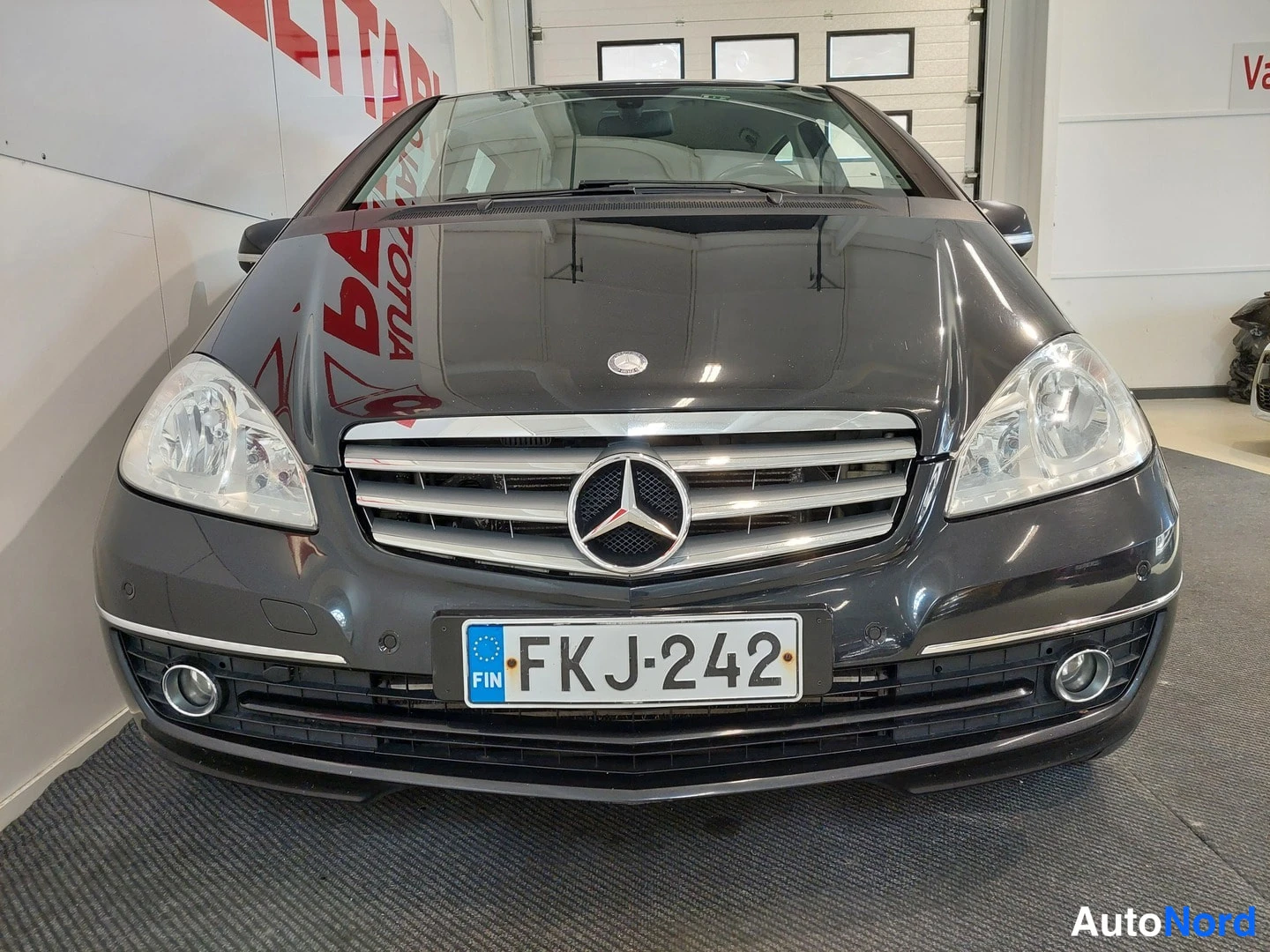 Edestä: Auton keula edestä: tumma Mercedes-Benz, rekisteritunnus.