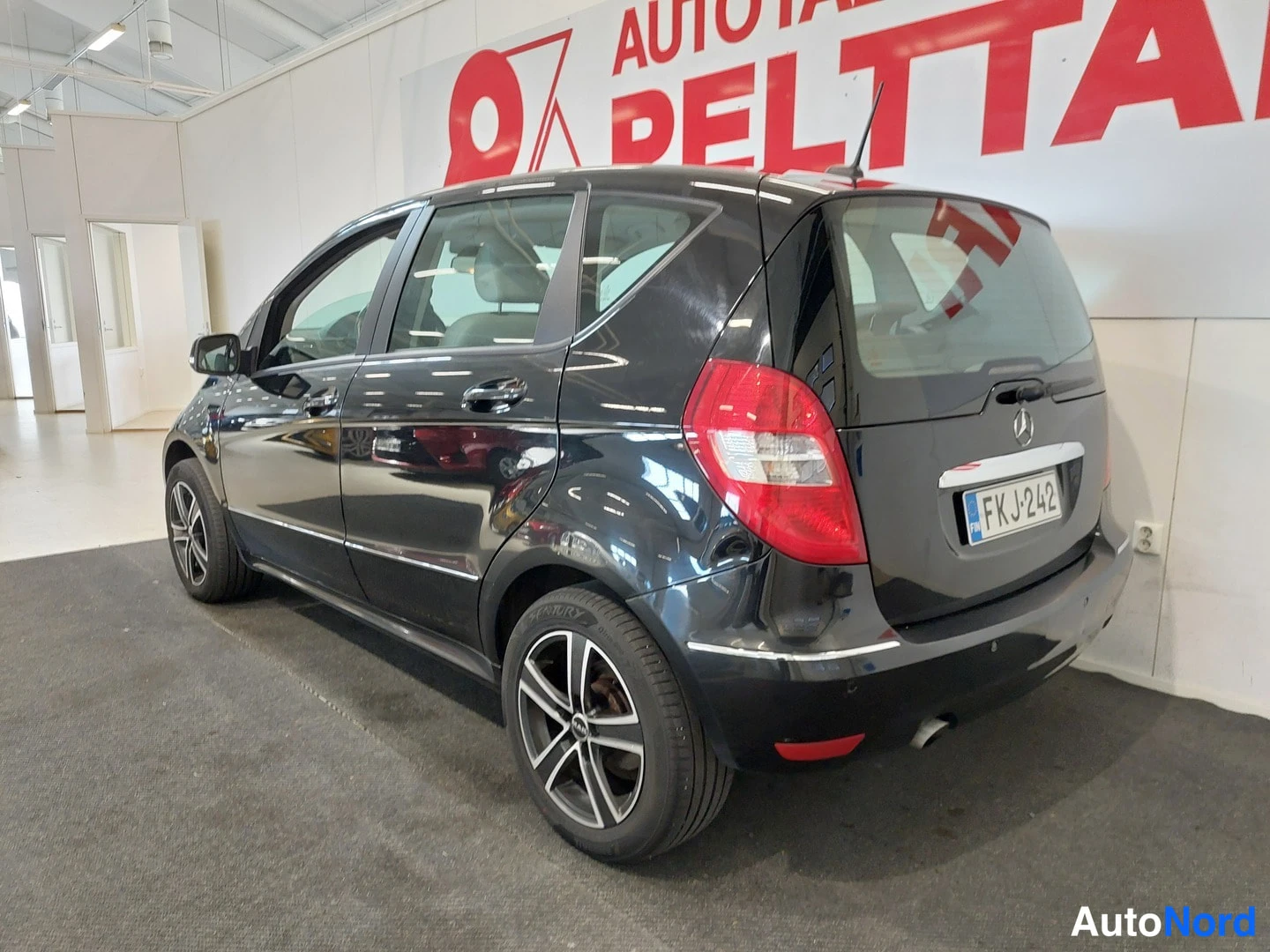 Takaviisto: Mustan Mercedes-Benz A -mallin takakulmakuva autovahvistamossa, takavalot ja rekisterikilpi näkyvissä.