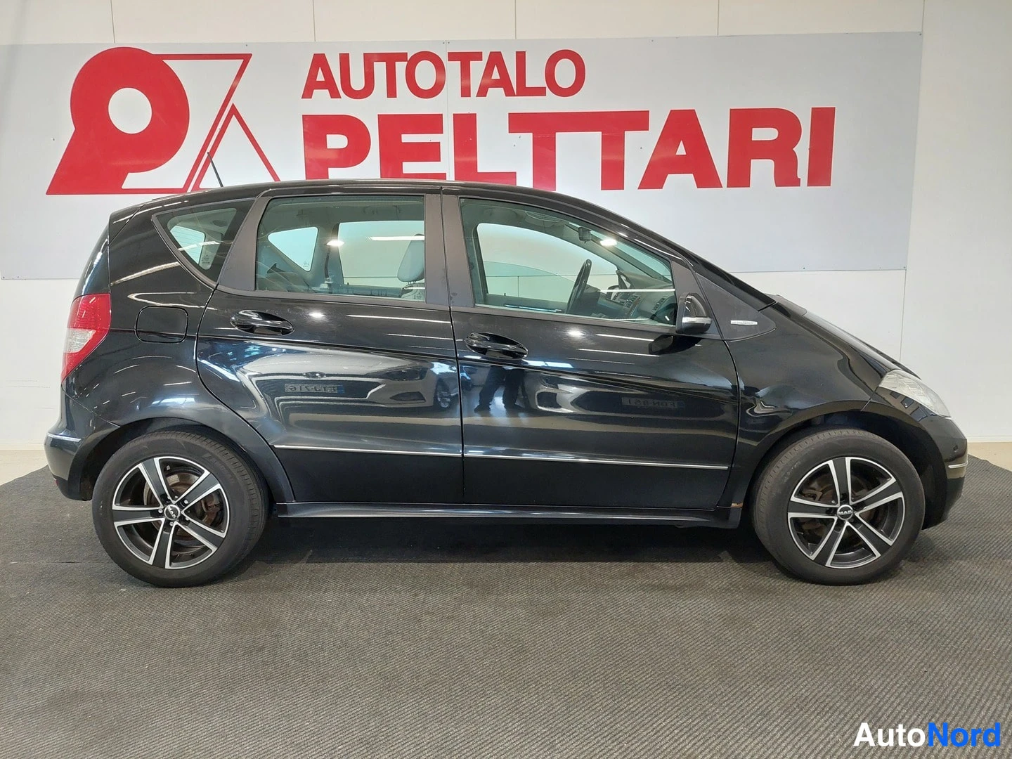 Sivulta: Musta Mercedes-Benz A-sarjan viisiovinen hatchback sivulta vasemmalta katsottuna autosalissa.