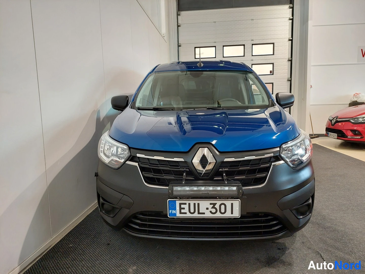Edestä: Renault-pakettiauto suoraan edestä, tummansininen kori, Renault-merkki keulassa, lisävalo puskurissa ja rekisteritunnus.