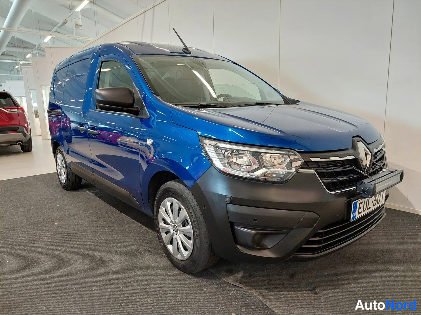 Etuviisto, nokka oikealle: Sininen Renault-pakettiauto etuviistöltä oikealta, etusäleikkö, ajovalot ja rekisterikilpi näkyvissä.