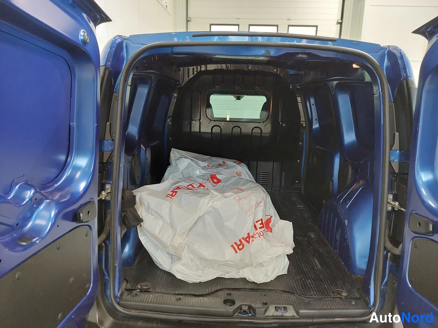 Takaa: Pakettiauton takaosassa auki olevat takaluukut paljastavat tyhjän mutta täyteen paneloidun lastaus- tilan, jonka lattialla on valkoinen muovikassi.