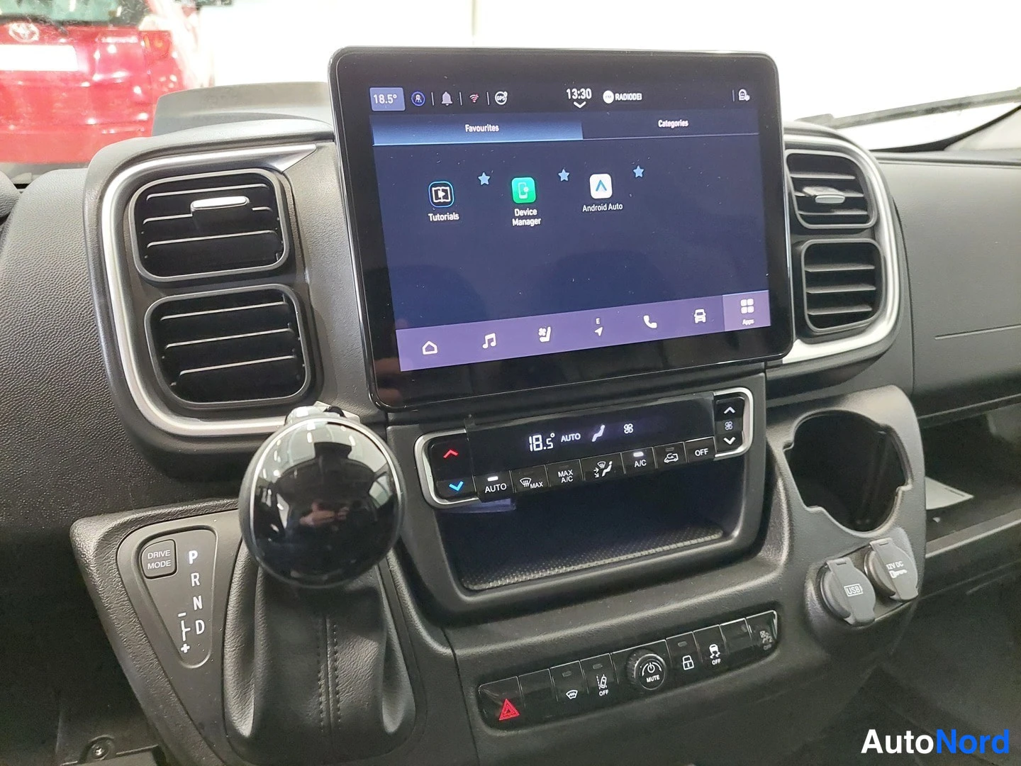 Muu: Kojelauta, jossa telineessä oleva infotainment-näyttö näyttää valikkoa, jossa ovat Tutorials, Device Manager ja Android Auto, sekä automaattista ilmastointia oh