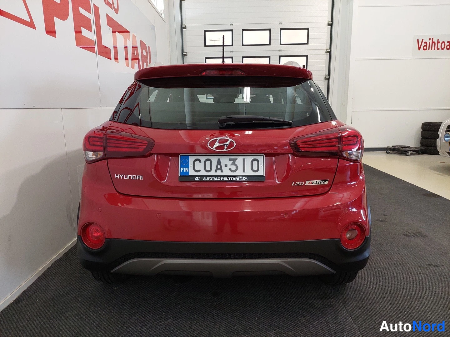 Takaa: Auton takaosa suoraan takaa: punainen Hyundai i20, rekisterikilpi, takavaloissa tummat ohjelmointi-ikkunat ja takapuskurissa tumma suoja.