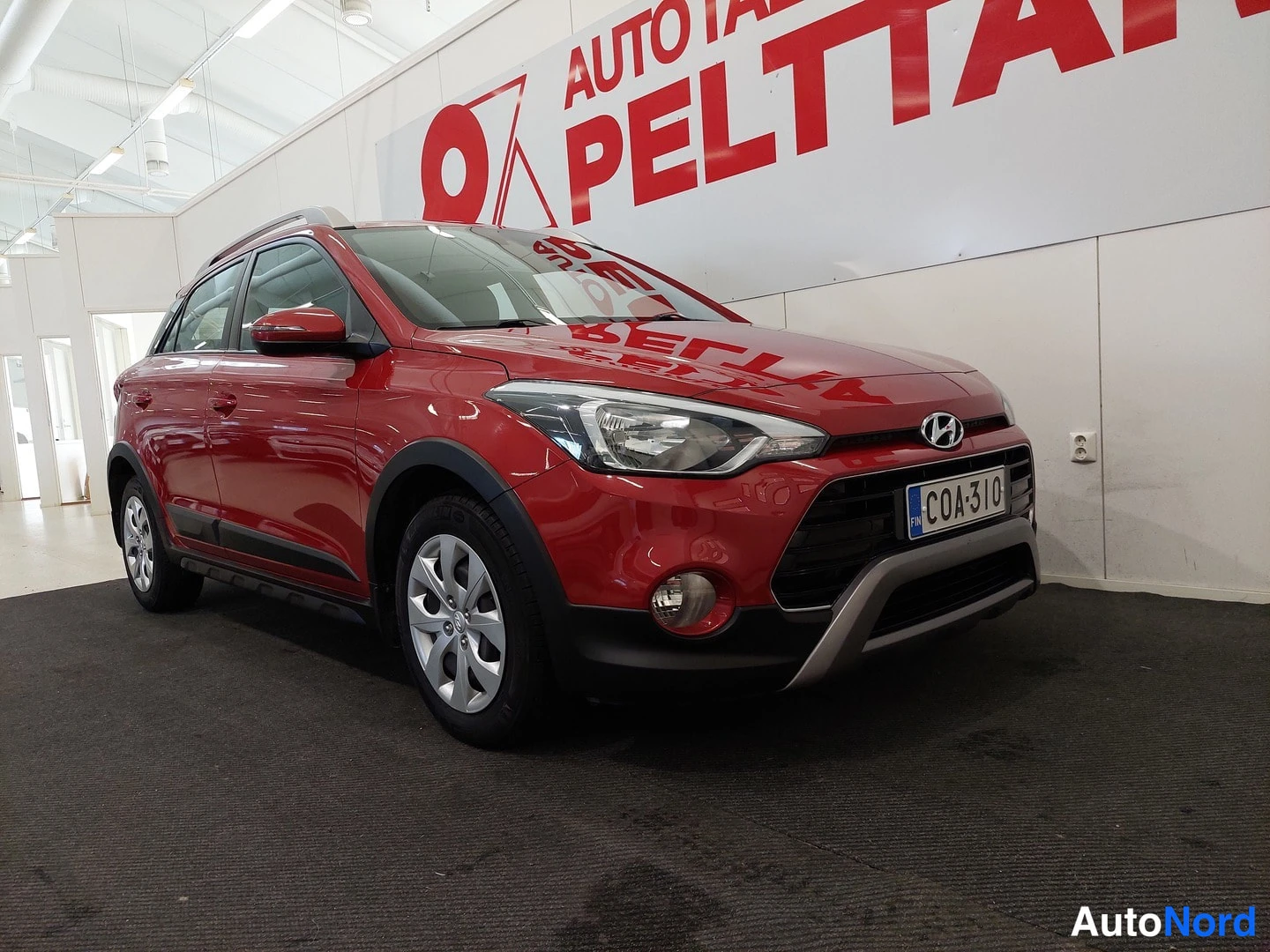 Etuviisto, nokka oikealle: Punainen Hyundai i20 Active Cross etuviistöstä ostonäyttelytilassa, rekisterikilpi.