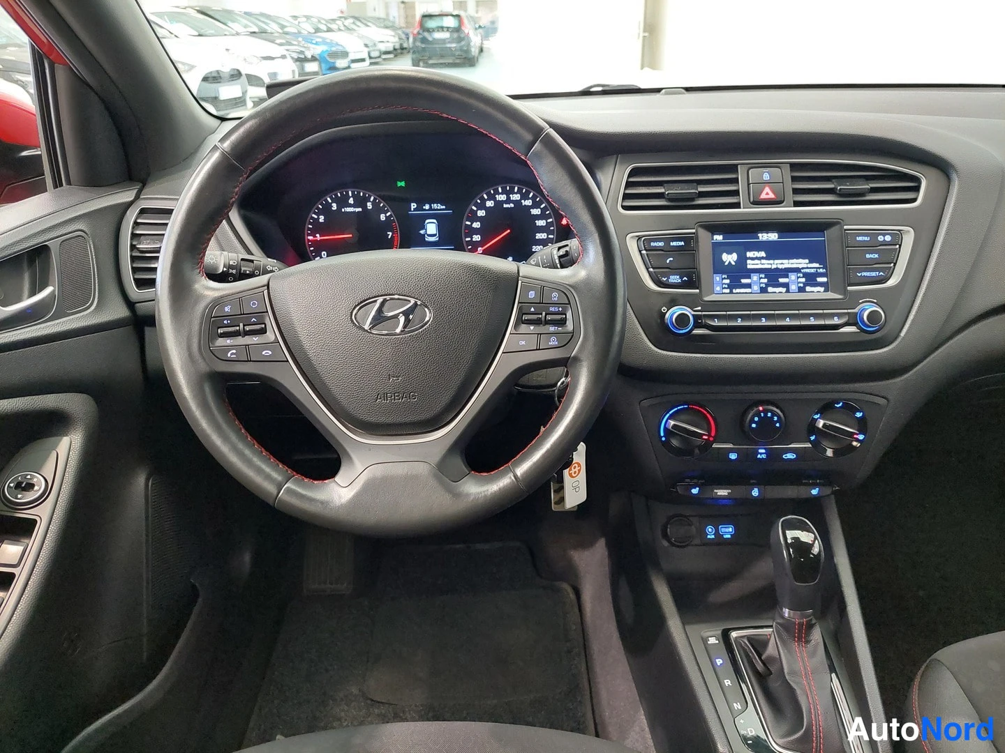Muu: Kuljettajan näkymä Hyundai i20:n ohjaamoon: monitoimiohjauspyörä, mittaristo ja keskikonsolin näyttö, automaattivaihteen keila.