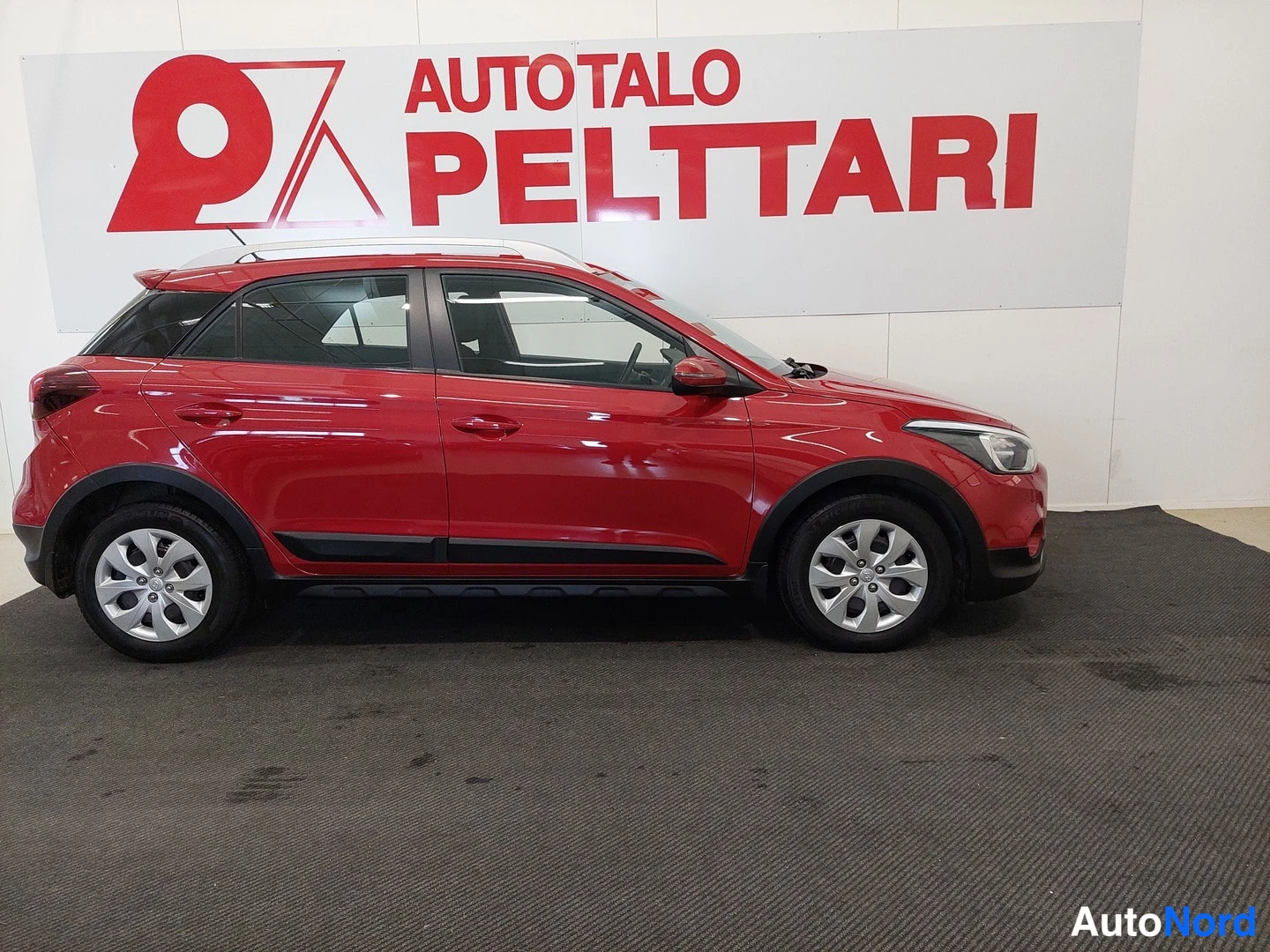 Etuviisto, nokka oikealle: Punainen Hyundai i20 Active Cross sivulta etunurkkaan, Autotalo Pelttari-tausta