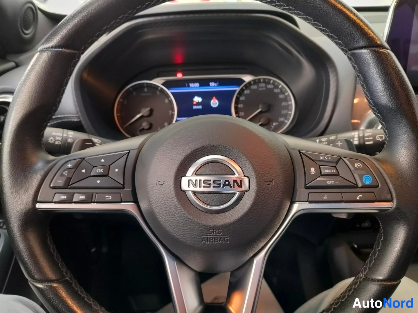 Muu: Nissan-ohjauspyörä ilmastointilaitteineen ja -painikkeineen (RES+, CANCEL, SET), mittaristo taustalla.