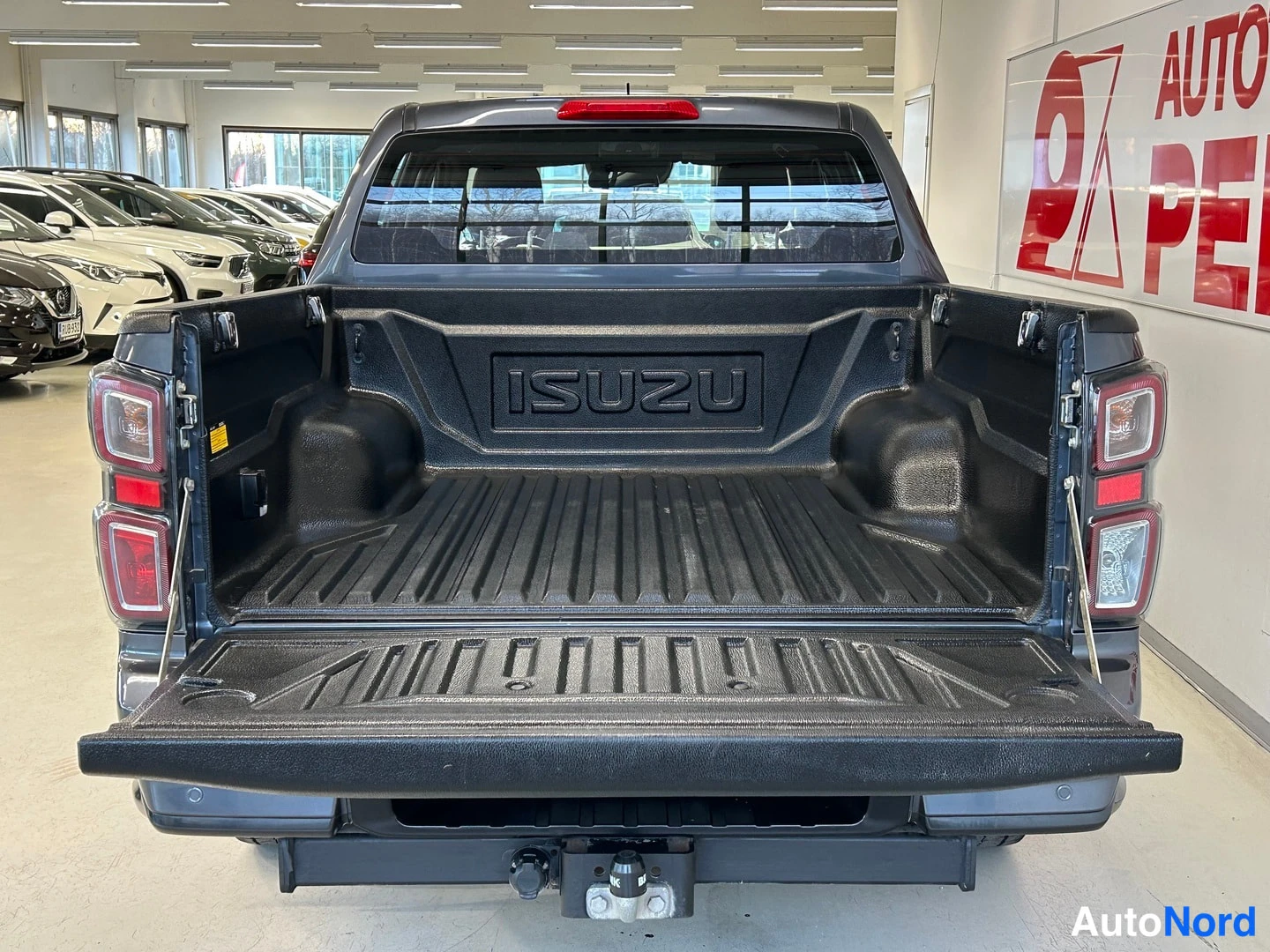 Takaa: Isuzu D-Max lavalla avattu takaluukku: lavan sisus ja ISUZU-teksti näkyvät, auto tummanharmaa.