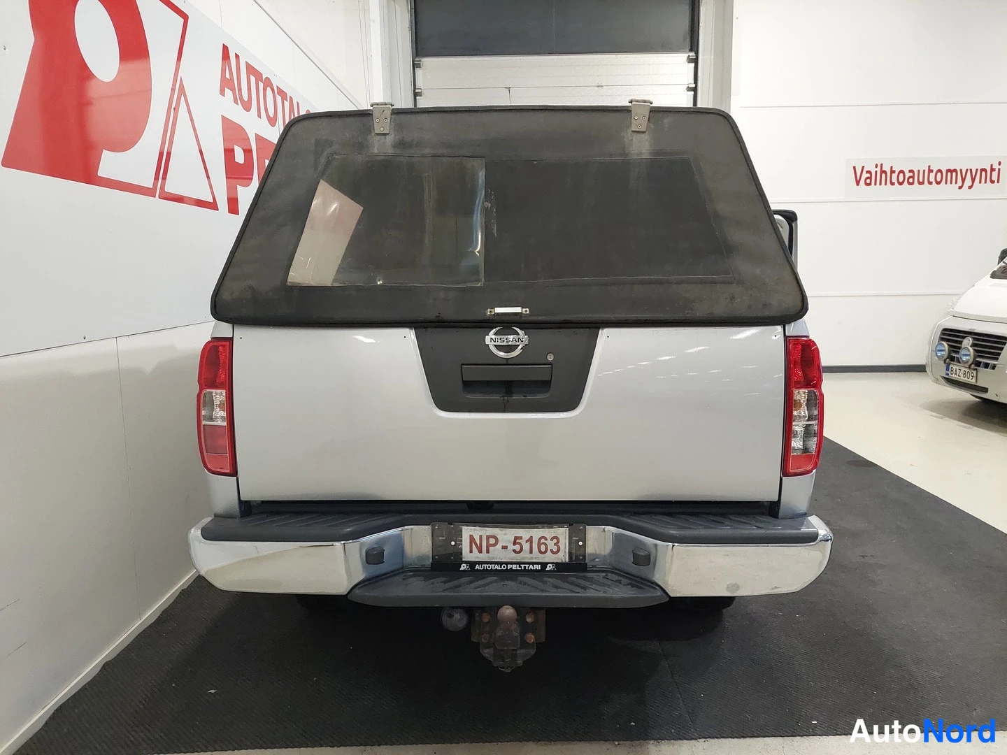 Takaa: Nissan Navaran takaosa suoraan takaa: hopeinen koripaneeli, punaiset takavalot, kromattu puskuri ja rekisteri NP-5163; tumma kuormasuoja kannessa ja vetokoukku